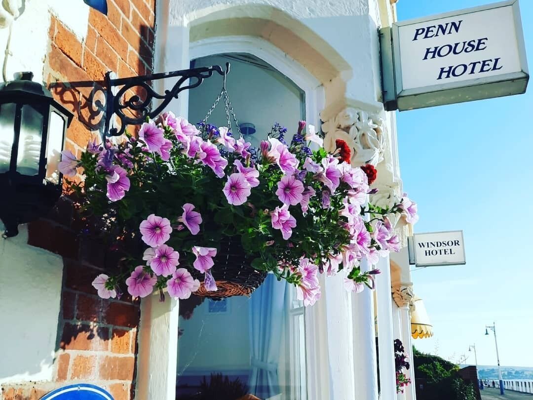 Een bloemenmand met roze bloemen voor een gebouw met een bord waarop staat: "Penn House Hotel".