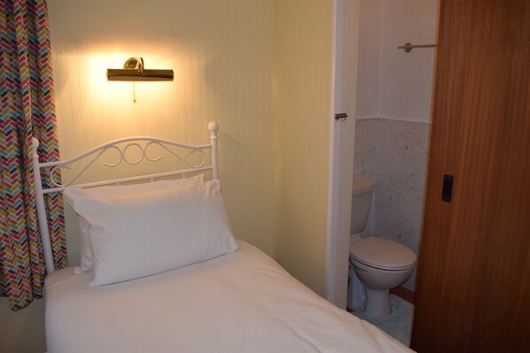 A small, private room with a single bed, a bedside table, a wall-mounted light, and a toilet. - Penn House Hotel (Weymouth)