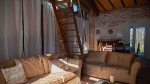 A rustic living room with two sofas, a ladder, a brick wall, and a dining area with a table and chairs.