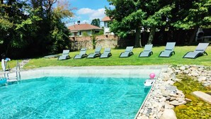 A clear swimming pool with lounge chairs and a stone border.