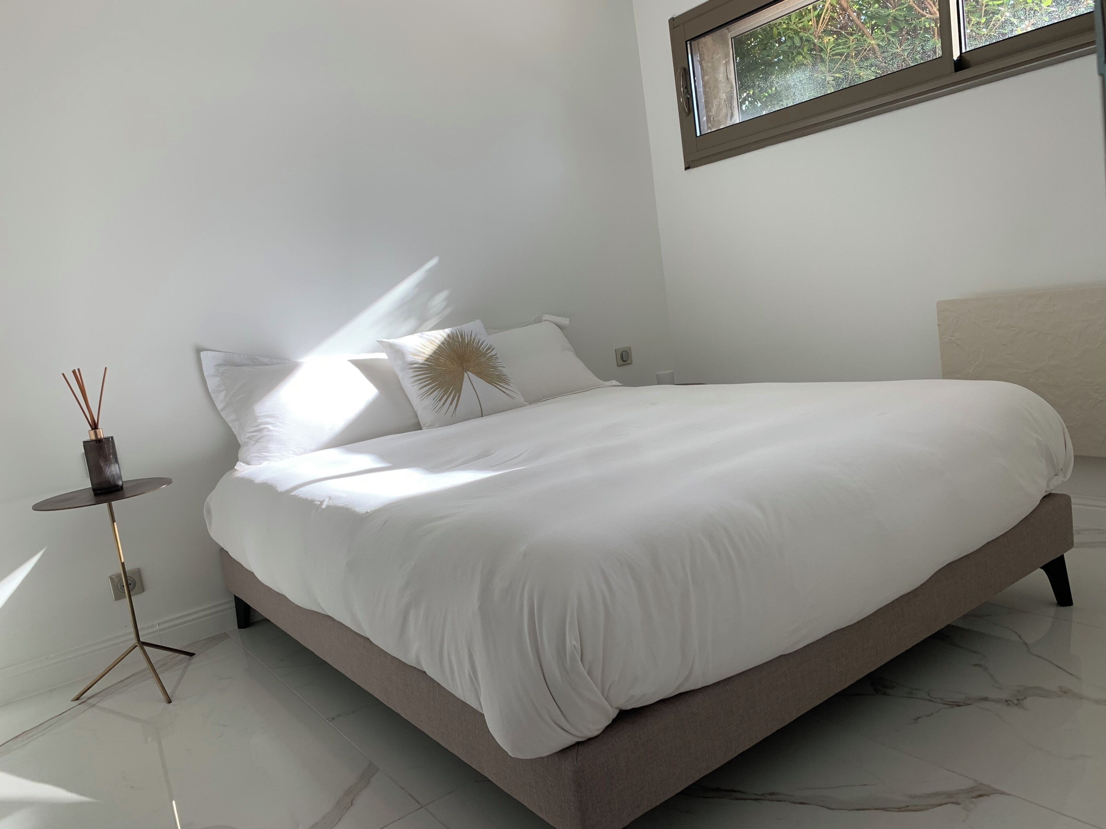 Une chambre moderne avec un grand lit, une petite table de chevet et une fenêtre donnant sur un paysage verdoyant.