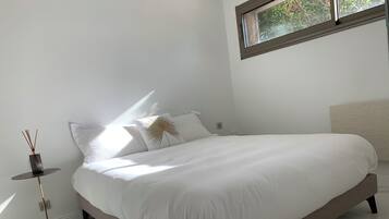Een moderne slaapkamer met een groot bed, een klein nachtkastje en een raam met uitzicht op groen.