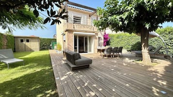 Een huis met twee verdiepingen, een terras, tuinmeubilair en een tuin.