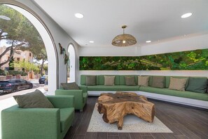 Zona d'estar moderna amb sofàs verds, taula de centre de fusta i una paret amb un mural de fullatge verd.
