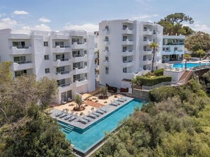 Un hotel modern amb diversos edificis blancs, una piscina i un jardí paisatjistic.