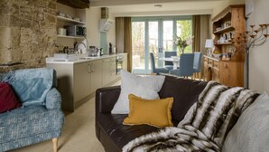 A cozy living room with a sofa, a coffee table, and a dining area with chairs and a table. - The Hall - luxury barn conversion in the Cotwolds (Bristol)