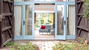 A rustic barn-style entrance with a glass door leading to a patio area with outdoor seating. - The Hall - luxury barn conversion in the Cotwolds (Bristol)