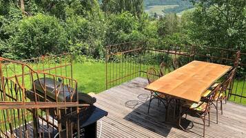 Una terraza de madera con una mesa y sillas, rodeada por una valla metálica, con vistas a un paisaje verde exuberante.