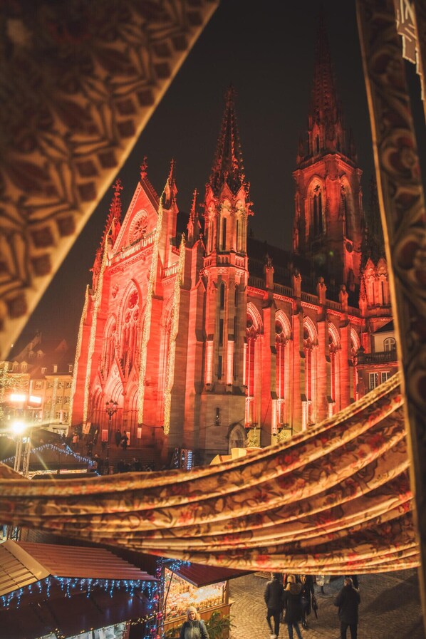Una catedral de estilo gótico iluminada con luces rojas, y una calle con gente caminando abajo.