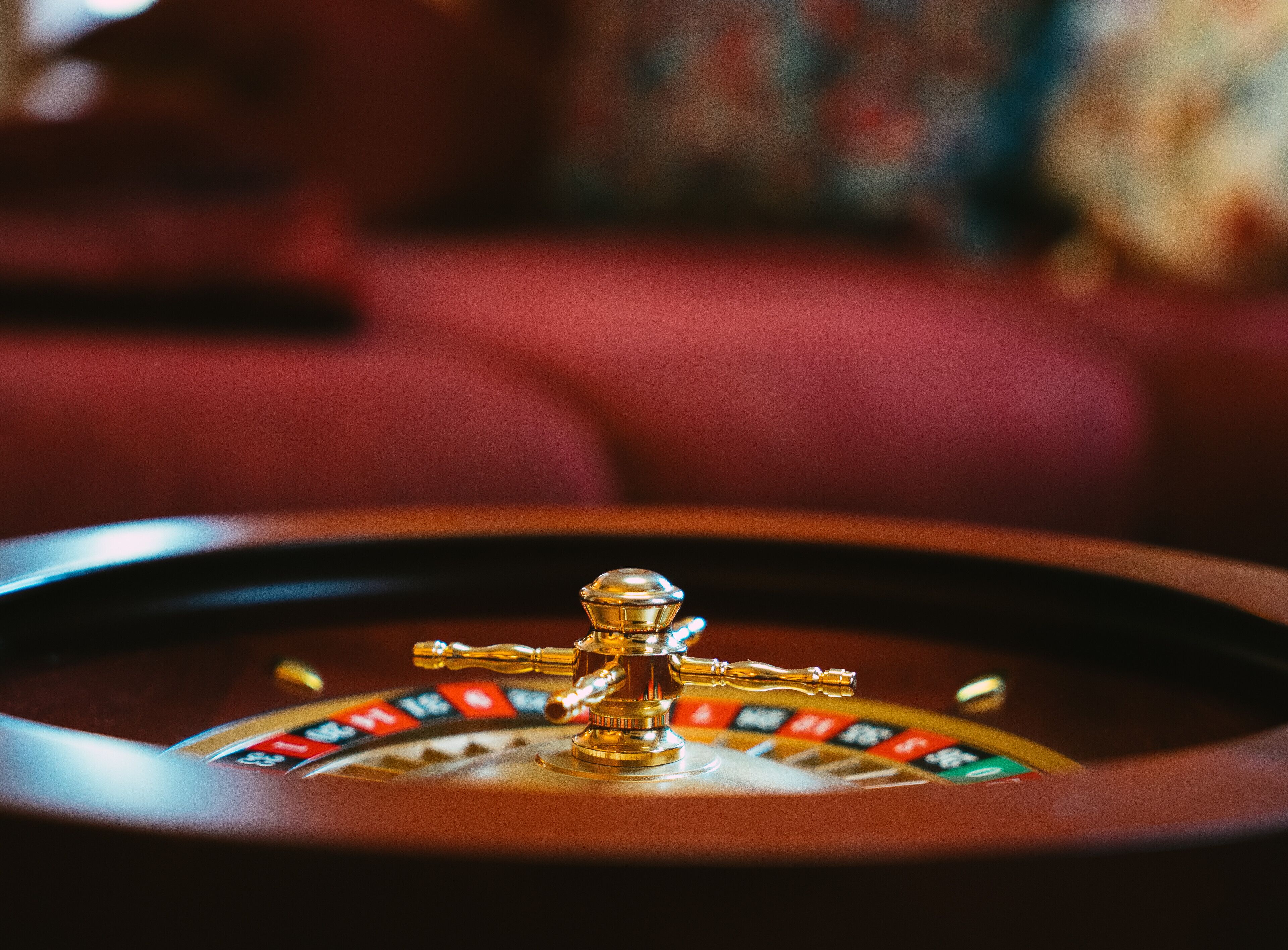A roulette wheel with a golden ball in motion, set against a blurred background of a red couch.