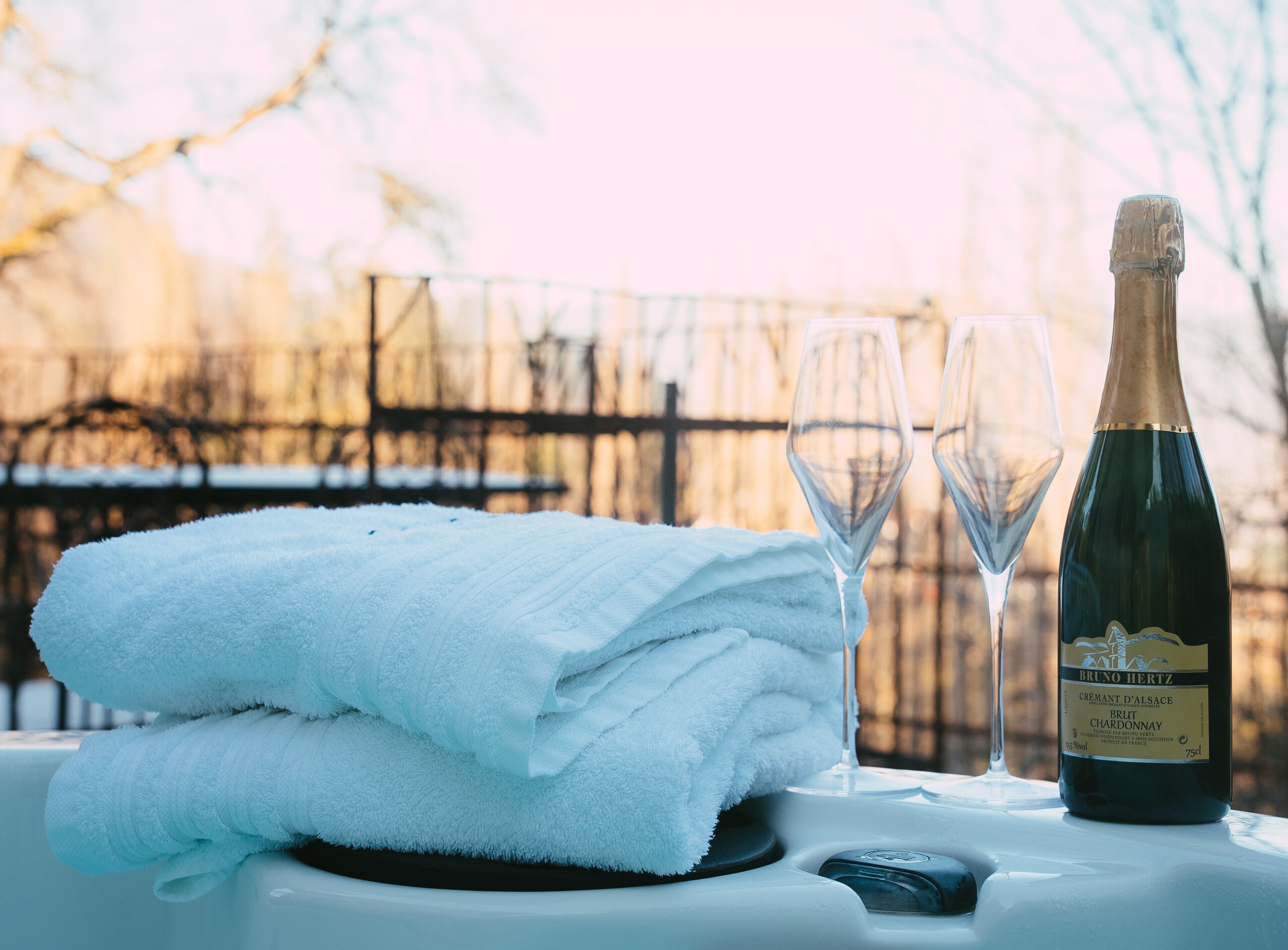 En flaska Bruno Hertz Crémant d'Alsace Brut Chardonnay och två glas på ett bord, tillsammans med en hopvikt vit handduk.