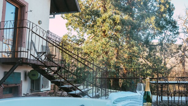 Un bain à remous avec une bouteille de champagne et des serviettes, un escalier menant à un balcon et une vue sur les arbres.