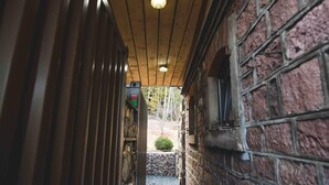 Un couloir étroit avec des poutres en bois au plafond et des murs en briques, qui mène à un petit espace extérieur doté d’un mur en pierre et d’un arbuste.