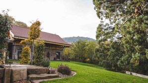 Un bâtiment en pierre, surmonté d’un toit en tuiles, entouré d’une pelouse bien entretenue et d’arbres.