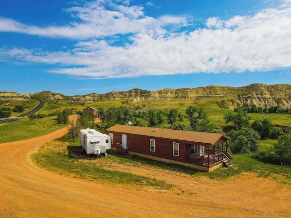 A single-story house with a porch, a detached RV, and a dirt road.