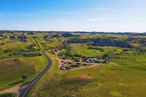 A rural landscape with a winding road, green fields, and a few buildings.