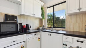 A modern kitchen with white cabinets, a black countertop, a microwave, a coffee maker, a dishwasher, and a washing machine. - River Suite.  Rest, Revitalise, Relax (Maylands)