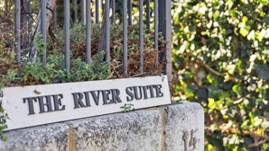 A sign for "The River Suite" with a stone base and metal fence in the background. - River Suite.  Rest, Revitalise, Relax (Maylands)