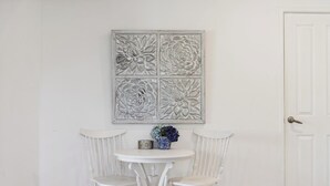 A room with a white door, a white wall, a white round table with two white chairs, and a floral artwork above the table. - River Suite.  Rest, Revitalise, Relax (Maylands)
