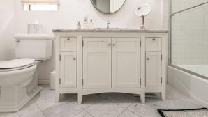 A bathroom with a toilet, a white vanity with three cabinets, a mirror, and a shower area. - "Contemporary townhouse-style condo in West Hollywood." (Los Angeles)