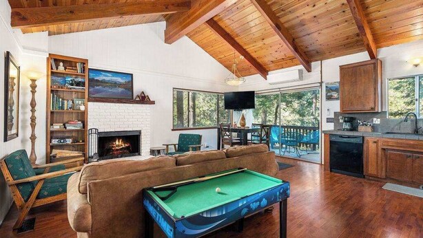 Un salon chaleureux avec une table de billard, une cheminée et une grande fenêtre donnant sur une terrasse.
