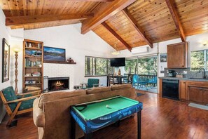 Un salon chaleureux avec une table de billard, une cheminée et une grande fenêtre donnant sur une terrasse.