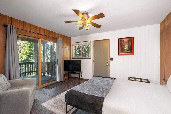Une chambre à coucher comprenant un lit, un ventilateur de plafond, une télévision et une porte-fenêtre coulissante donnant sur un balcon.