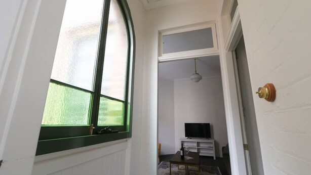 Un corridoio con un'ampia finestra ad arco, un televisore su un mobile e una porta con maniglia in ottone.