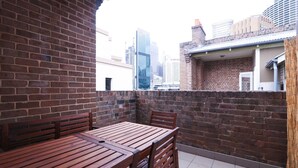 Un balcone con un tavolo e sedie in legno, pareti in mattoni e vista sulla città.