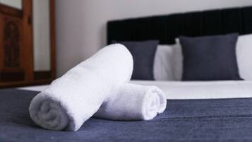 A neatly made bed with a dark blue bedspread and two rolled white towels.