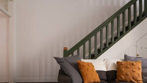 Un soggiorno con un divano grigio scuro, due cuscini color senape, un cuscino bianco e una scala in legno verde.