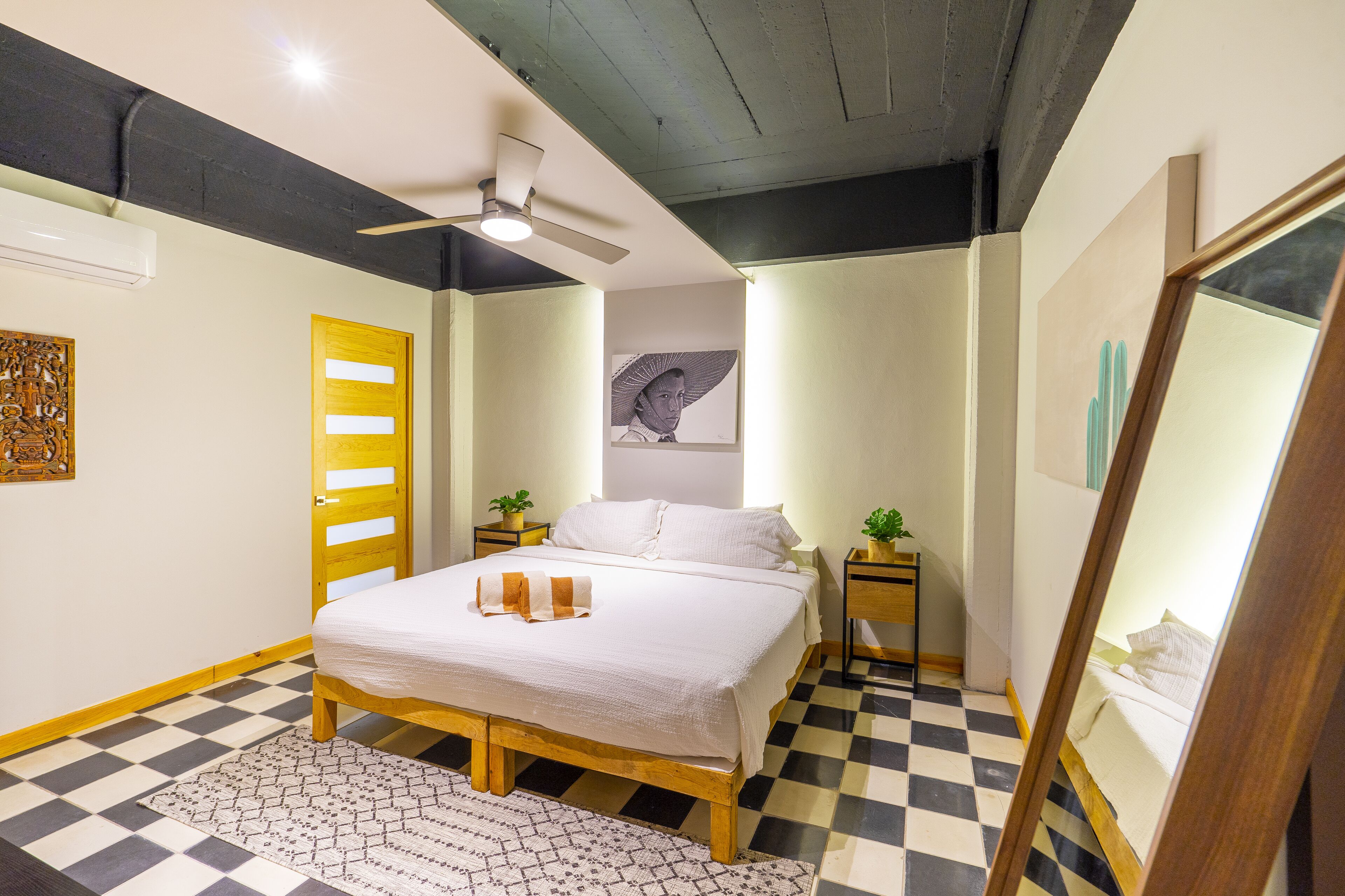 Un dormitorio con piso a cuadros, una cama con ropa de cama blanca, un ventilador de techo y una puerta de madera.