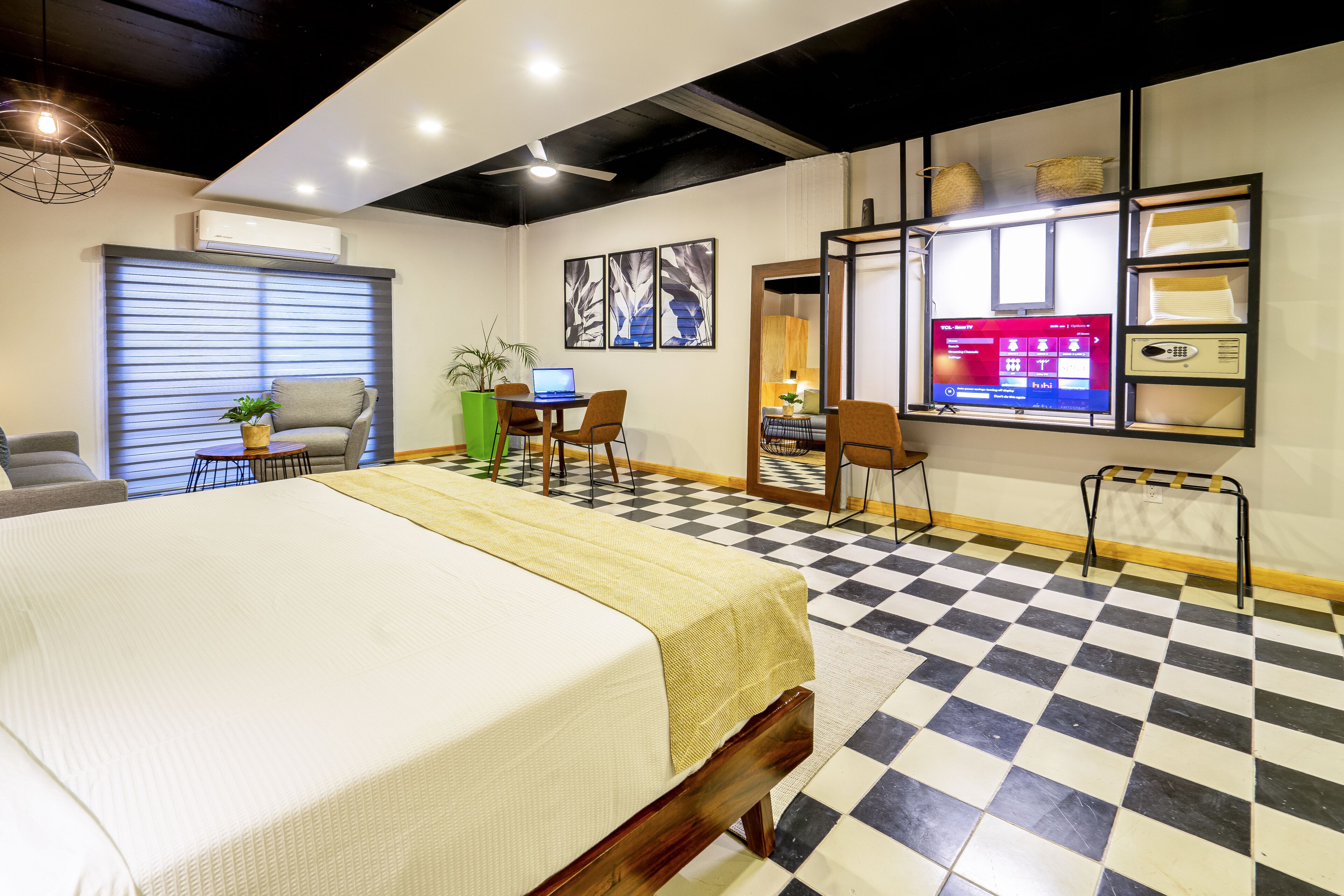 A hotel room with a large bed, a desk with a laptop, a TV, and a checkered floor.