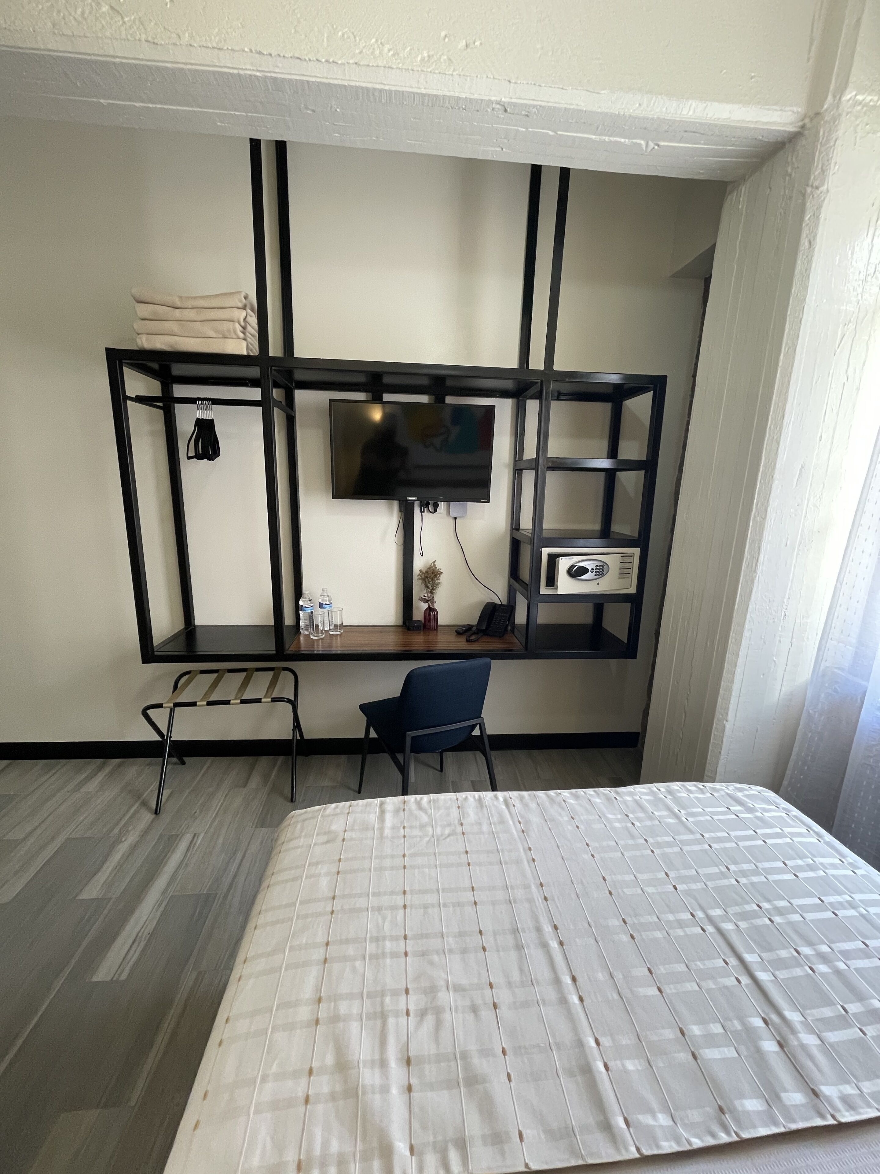 Une chambre d’hôtel comprenant un lit, un bureau avec une télévision, une chaise et une étagère avec divers objets.