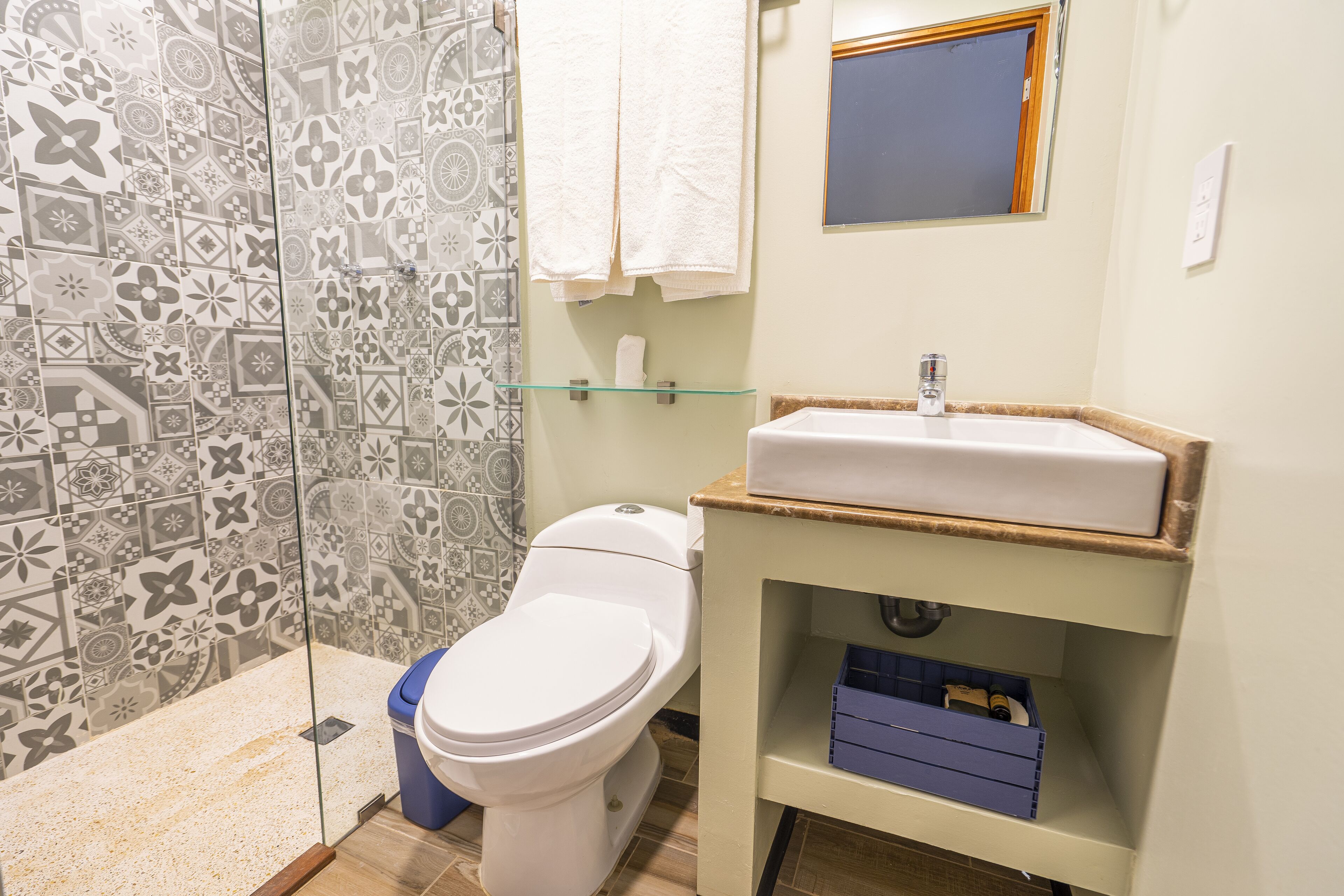 A bathroom with a toilet, a glass shelf with a towel, and a sink with a mirror above it.