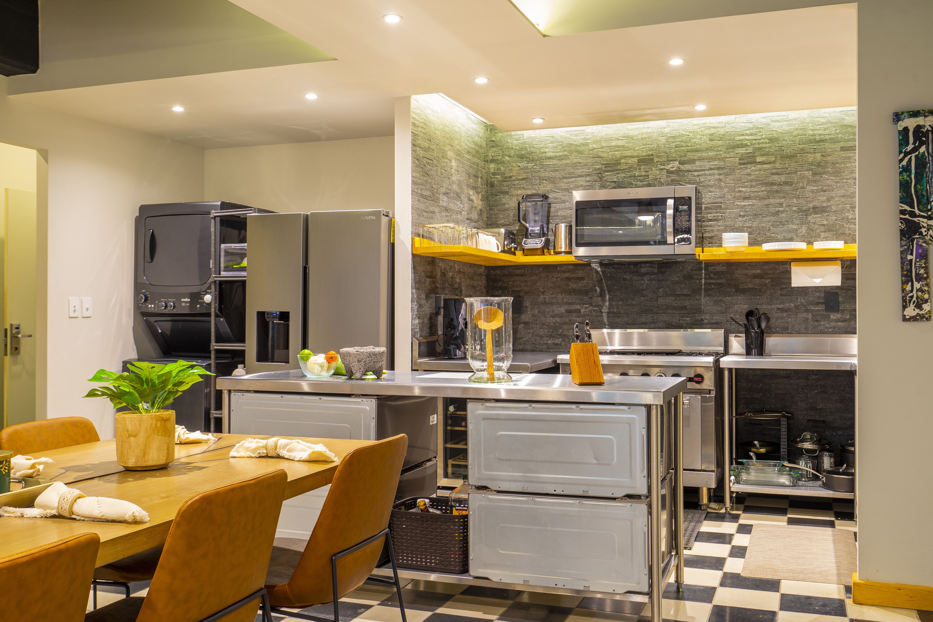 A compact kitchen with modern appliances, a dining area with a table and chairs, and a checkered floor.