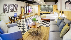 Een moderne hotelkamer met een zwart-wit geruite vloer, een bank, een eethoek en een kitchenette.