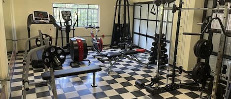 A gym with a checkered floor, weightlifting equipment, and cardio machines.