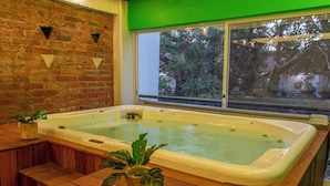 Een hottub in een houten terrasgedeelte met een bakstenen muur en een raam met uitzicht op begroeiing.