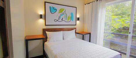 A bedroom with a large bed, a nightstand, a wall-mounted light, and a window with curtains.