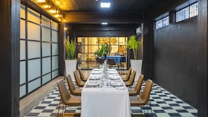 Een eetruimte met een lange tafel gedekt voor een maaltijd, omringd door stoelen, met een geruit vloertje en uitzicht op het interieur.