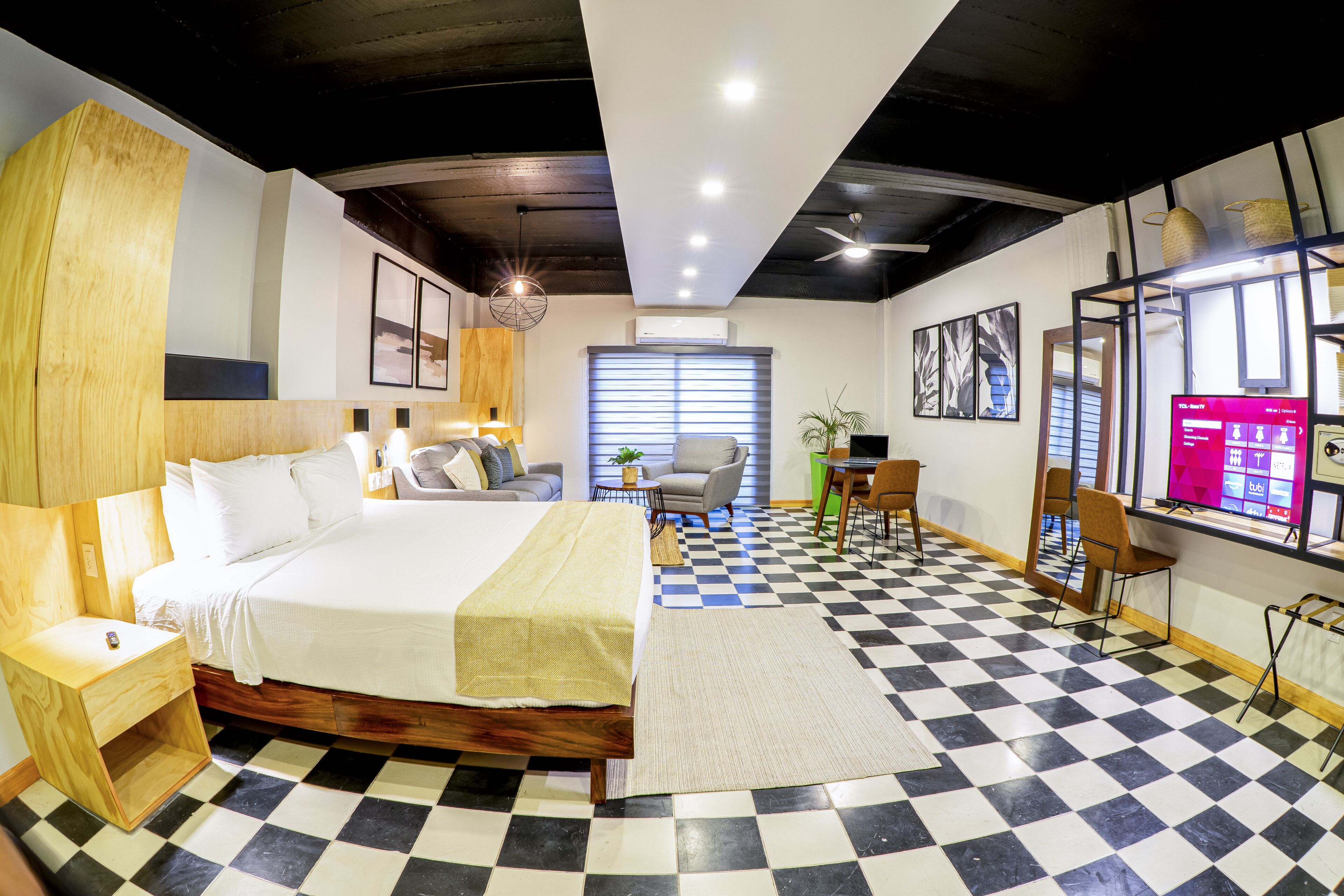 A modern hotel room with a checkered floor, a large bed, a desk, and a TV.