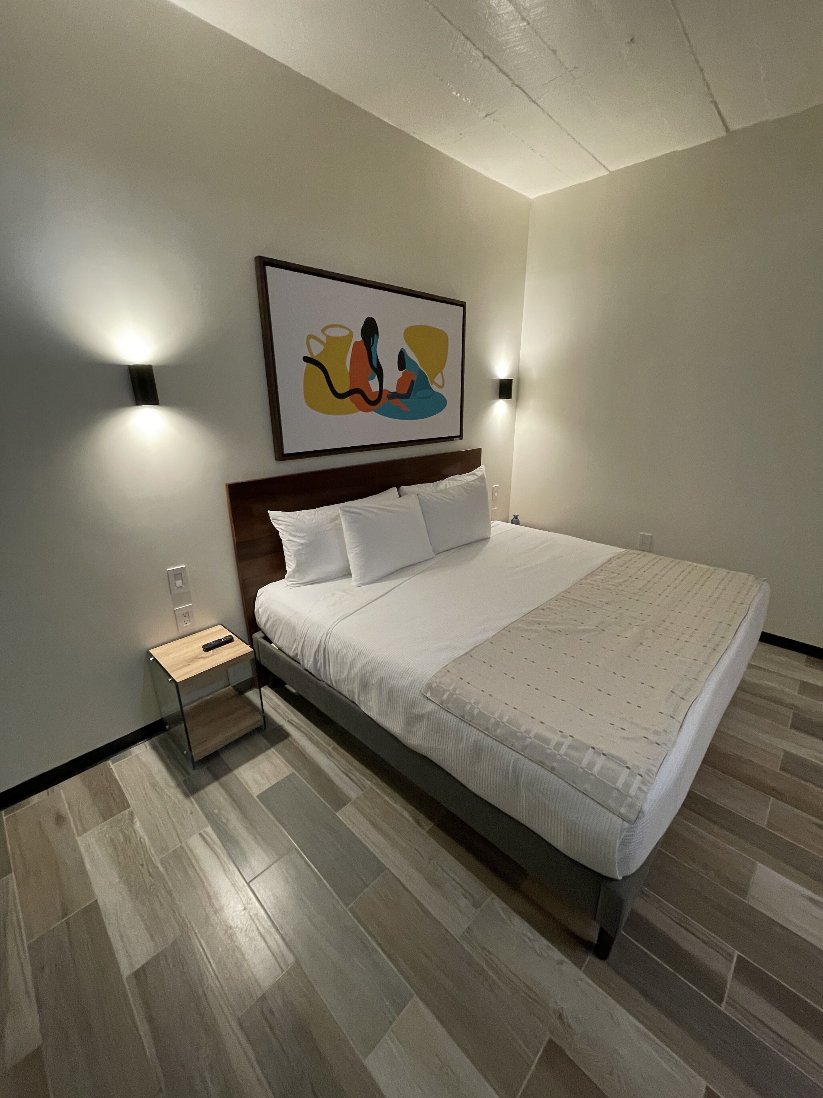Un dormitorio moderno con cama, mesita de noche y un cuadro abstracto colgado en la pared.