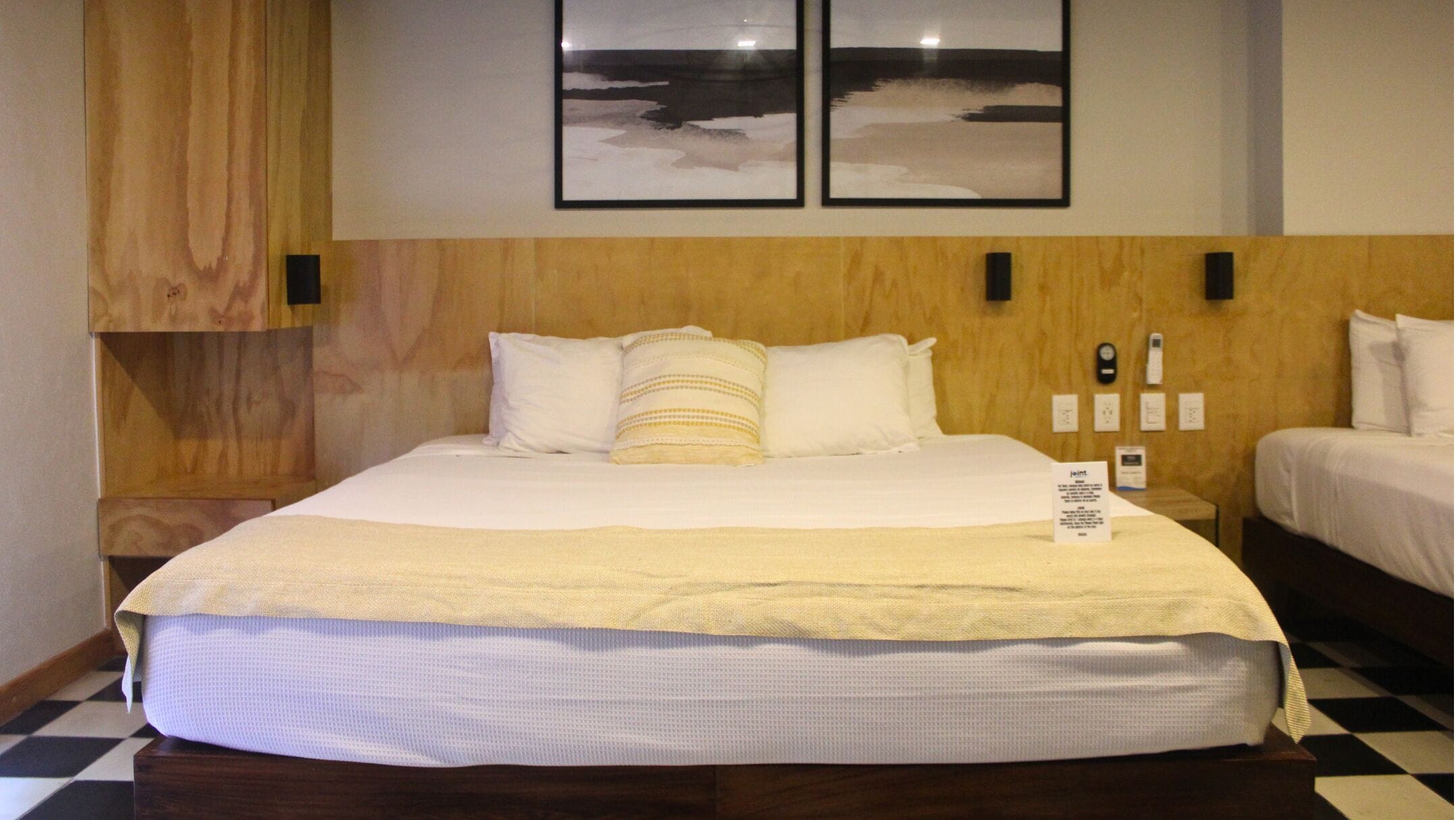 Ein Hotelzimmer mit einem großen Bett, zwei Kissen, einem Nachttisch und einem an der Wand befestigten Telefon.