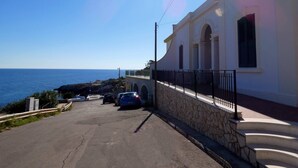 Una strada costiera con un edificio bianco, gradini in pietra e auto parcheggiate.