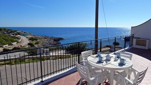 Un balcone con un tavolo apparecchiato per due, vista su una costa rocciosa e il mare.