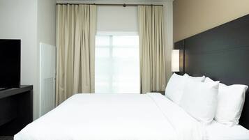 Quarto de hotel com uma cama grande, televisão de tela plana e uma janela com cortinas.
