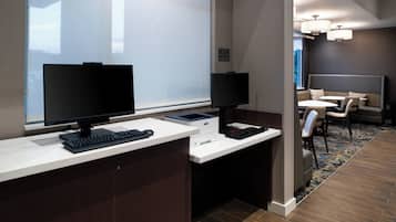A modern office space with two desks, each with a computer monitor, keyboard, and mouse. There is a seating area with a couch and chairs.