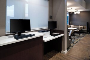 Un espacio de oficina moderno con dos escritorios, cada uno con monitor de computadora, teclado y ratón. Hay una zona de estar con un sofá y sillas.