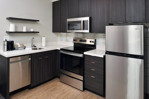 Una cocina moderna con armarios oscuros, electrodomésticos de acero inoxidable, microondas, horno y refrigerador.